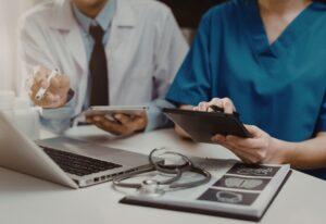 Healthcare professionals reviewing information on tablets during a consultation, with medical documents and a stethoscope on the table.
