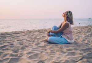 Person sitting on the sand at the beach at sunset, looking out toward the ocean.