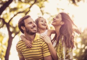 Smiling parents and young child enjoying time together outdoors in warm natural light.