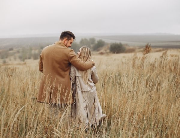 couple in field, man has his arm around the woman looking at each other smiling
